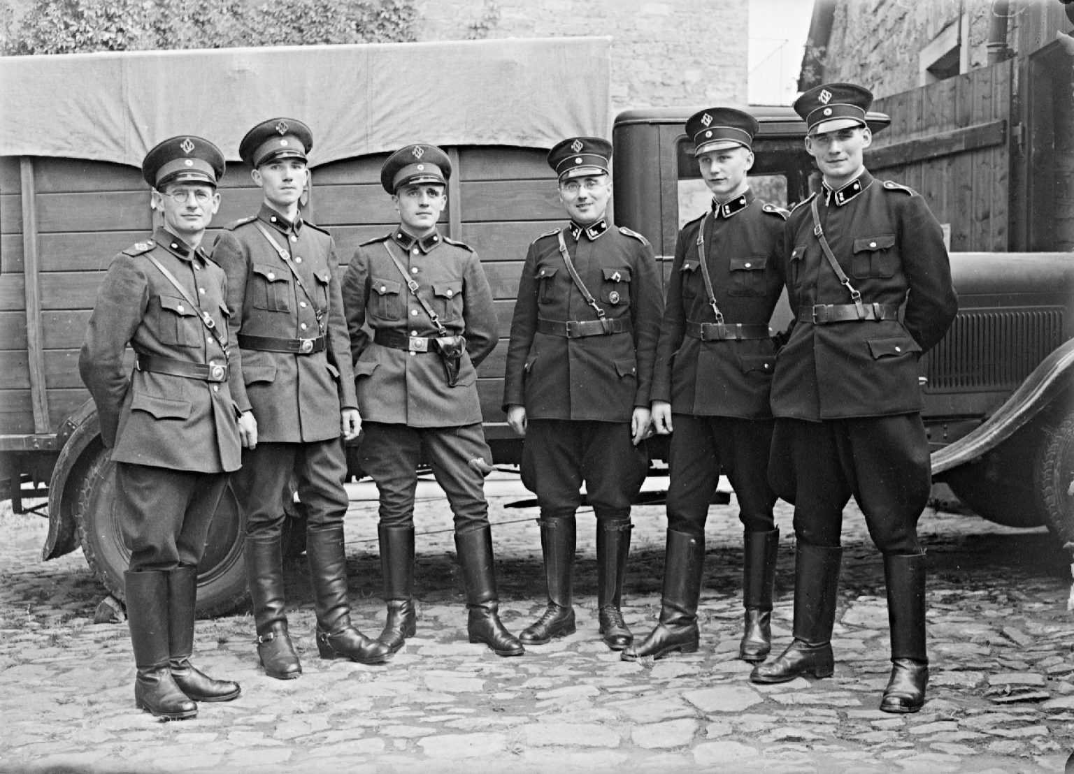 Historisches Schwarz-Weiß-Foto: sechs Wachmänner in Uniform vor einem Lastwagen