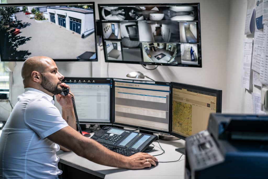 Mitarbeiter der Notruf- und Serviceleitstelle am Arbeitsplatz mit Monitorwand