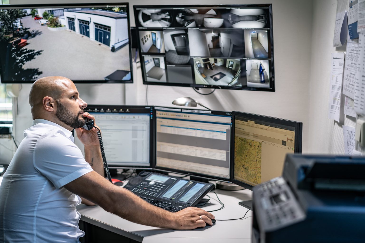 Mitarbeiter der Notruf- und Serviceleitstelle am Arbeitsplatz mit Monitorwand